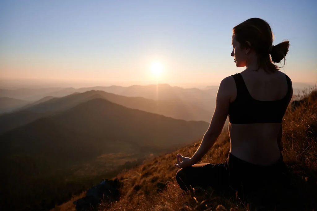 young woman meditating overlooking a mountain