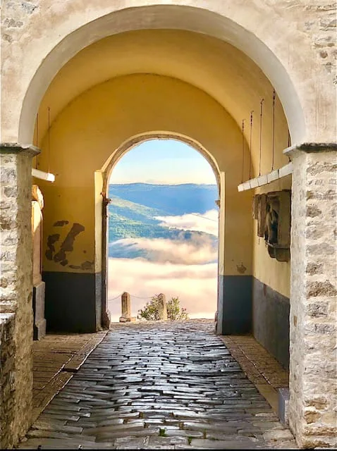 view from the cobblestone street in Motovun on yellow arches in front and the valley, fog and hills in the back