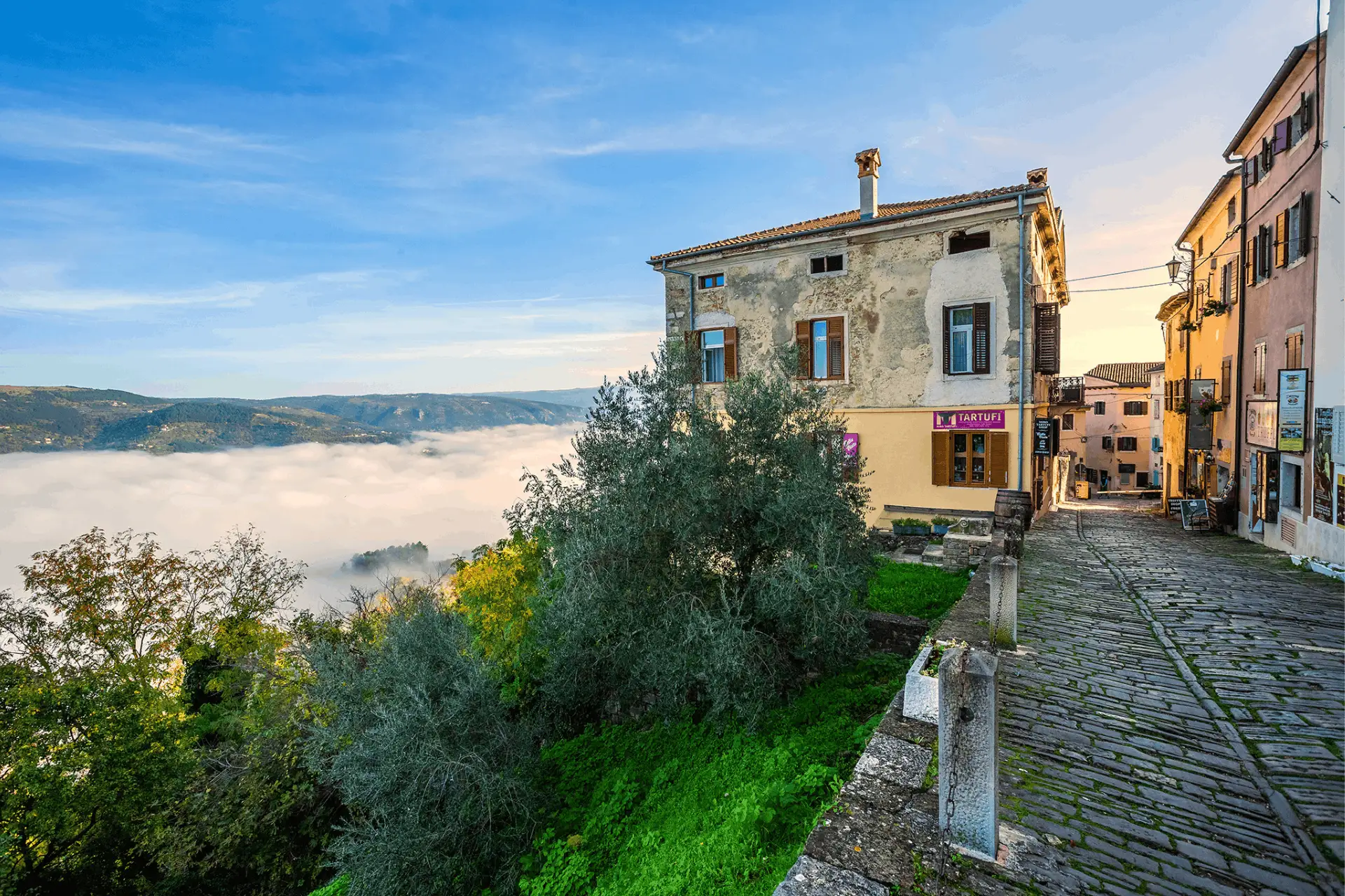 on the right side, a view on cobblestone street in Motovun and on the left is a valley engulfed in fog