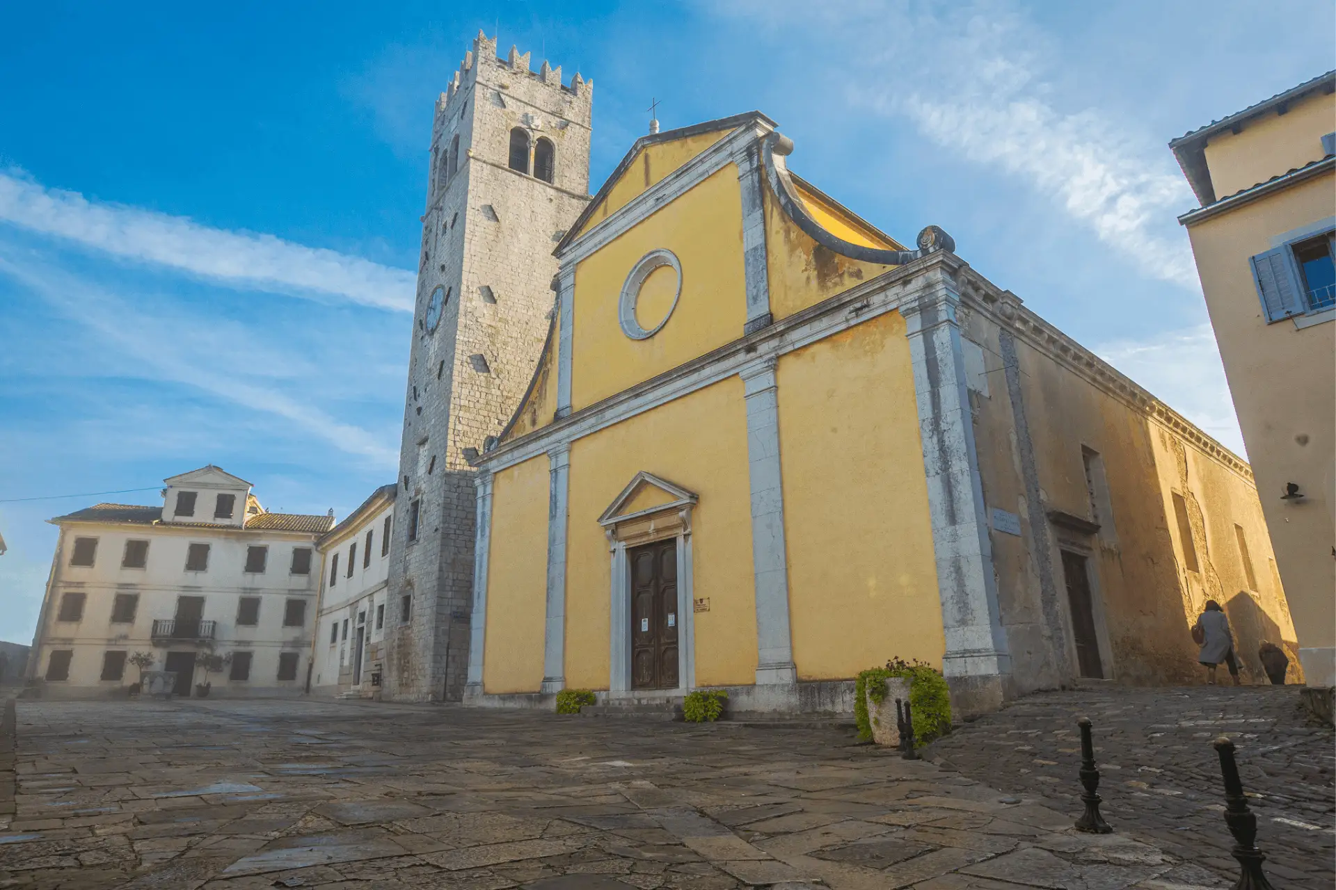 Motovun town square with an old yellow church and stone church tower