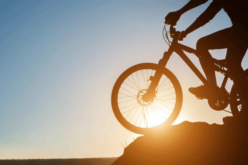 cyclist on a bike standing on a rock during sunset